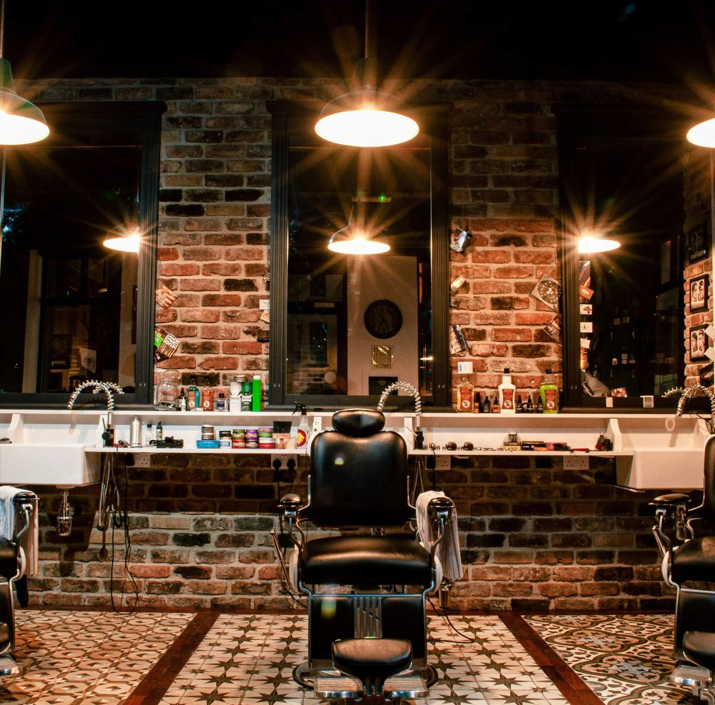 Barber chairs under hanging lights against a brick wall